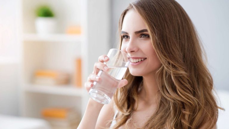 Woman smiling, drinking water indoors.