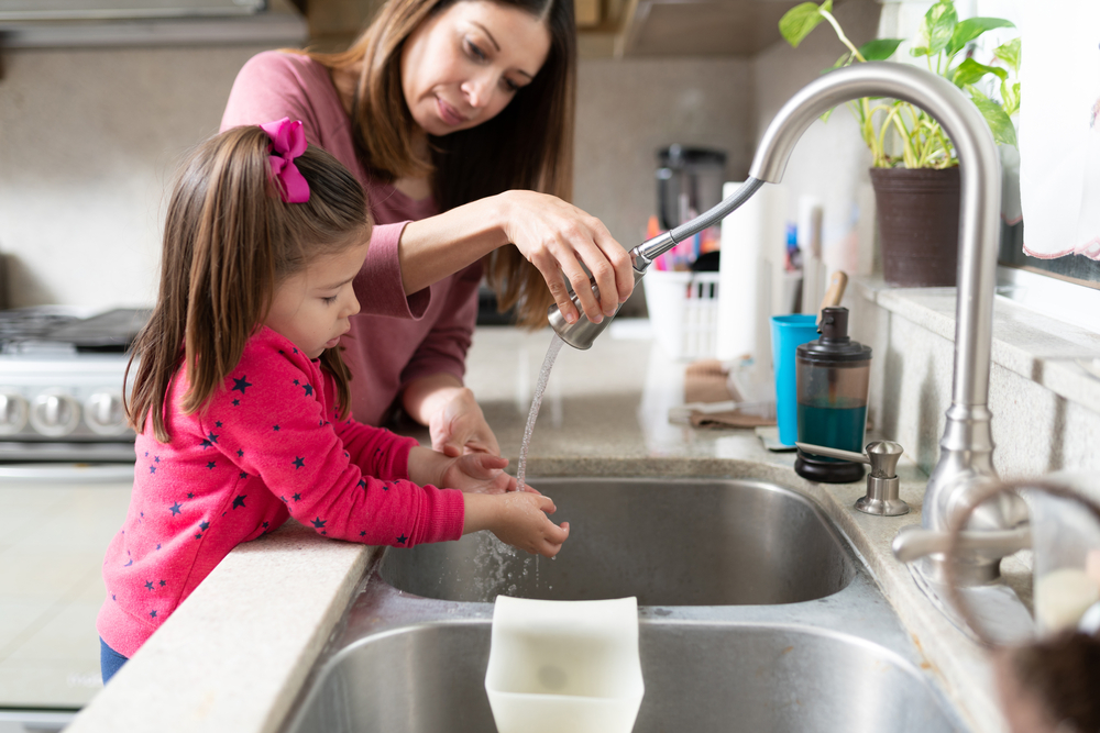 Mother and child washing hands in kitchen sink.